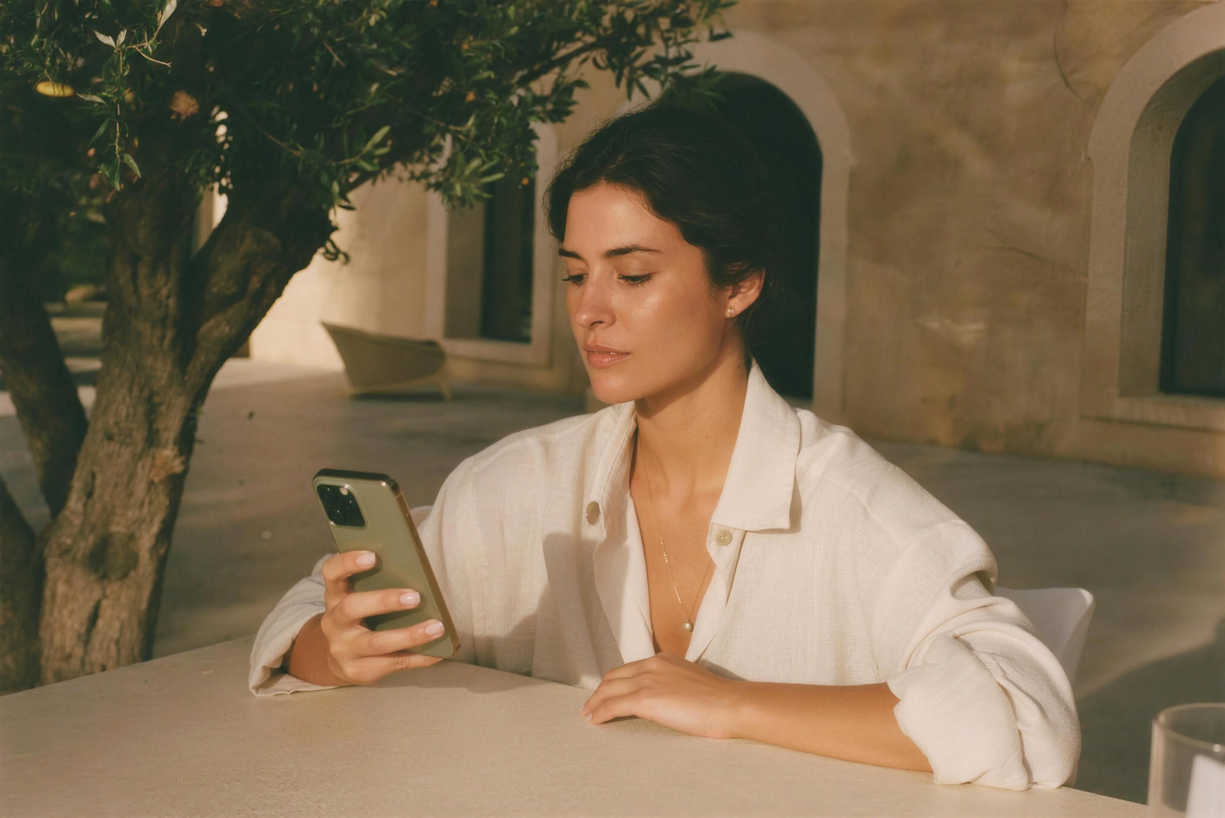 A woman reading on her phone at a sunlit stone terrace